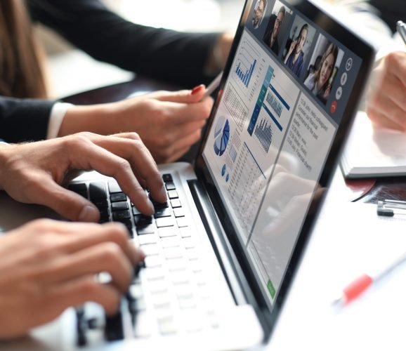 Business professionals working together at office desk, analyzing financial statistics displayed on the laptop screen. Webcam group conference with coworkers on laptop